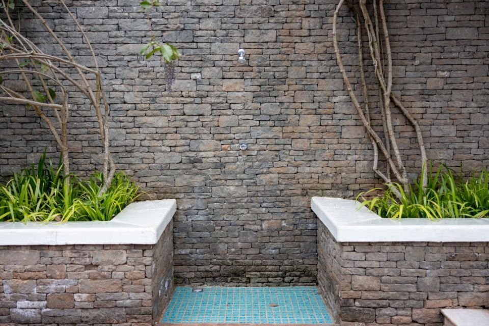 An outdoor shower with a stone wall and planters